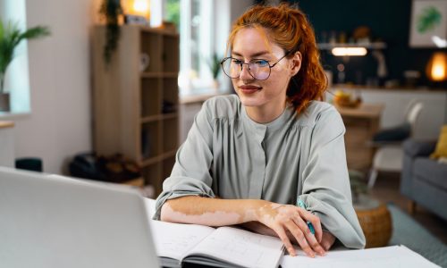 Young redhead Caucasian businesswoman or freelancer, with vitiligo and acne on her face, using laptop while working from home